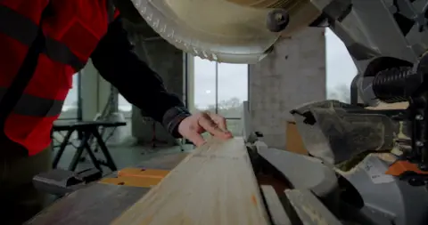 Strong saw/wood action frame with hands, tool, and material all readable.