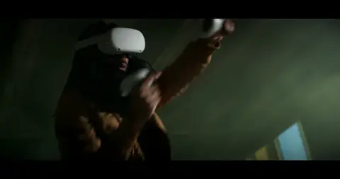 A person wearing a virtual reality headset moves through a dim green-lit room.