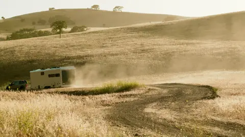 Strong dusty landscape action frame with trailer movement and strong outdoor context.