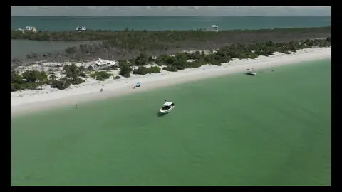 Strong coastal aerial with beach, water, and small boat context.