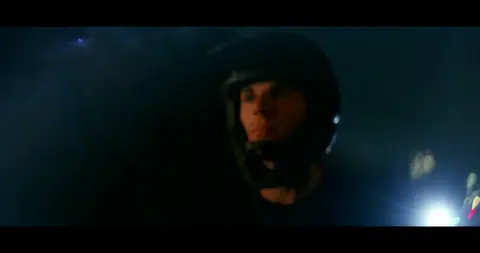 Strong low-light bike rider frame with face/helmet and cinematic lighting.