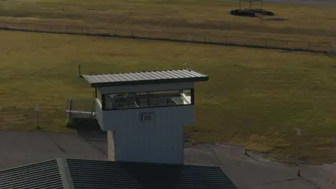 Strong elevated control-tower composition with graphic roof lines and track context.