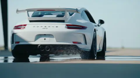 Strong rear Porsche action frame with readable vehicle shape, track spray, and acceleration.