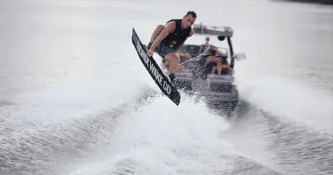 Strong wake rider action with clear rider, board, spray, and boat context.