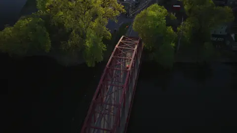 Top-down aerial of the red bridge, road, cars, nearby intersection, trees, and dark water.