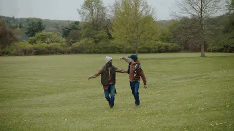 Two men move together, change direction and turn toward the camera across an open grassy field.