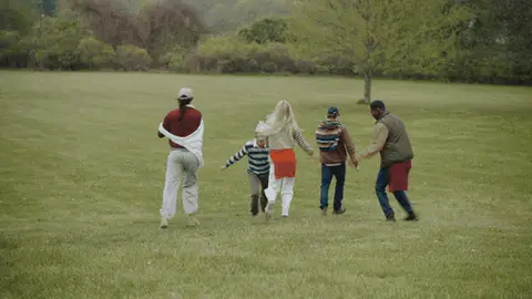 Five adults converge, turn and begin moving together across an open grassy field.