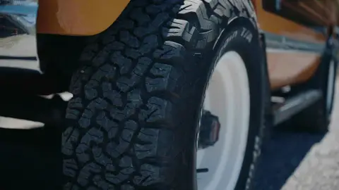 Deep tire tread and a white steel wheel fill the frame beneath the yellow fender of a vintage SUV.