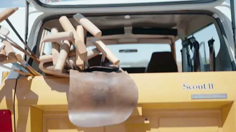 Wooden polo mallets rest across a brown leather saddle draped over a yellow vintage SUV tailgate below its open rear window.
