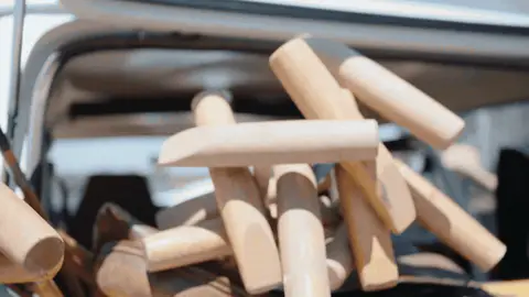 The camera moves across wooden polo mallets resting on a leather saddle beside yellow SUV bodywork.