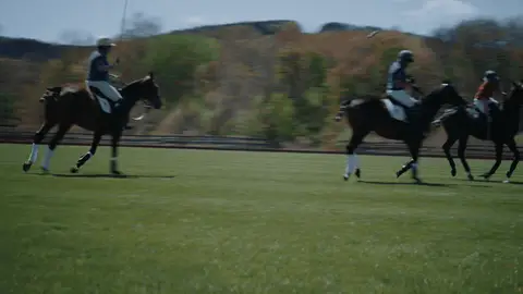Two mounted polo players move across a grassy field as one lifts a mallet during play.