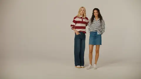 Two women pose together in burgundy-and-white and navy-and-white striped tops, one wearing jeans and the other a denim miniskirt.