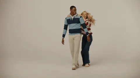 A woman in a burgundy striped top climbs onto a man in a navy striped rugby shirt for a playful piggyback ride in the studio.