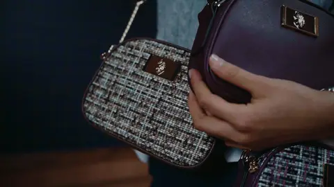 A hand rests across burgundy and multicolored tweed crossbody bags with gold-tone hardware and visible polo emblems.