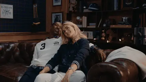 A woman leans toward a man on a leather sofa, then lifts her head as they smile.