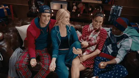 Four adults in colorful sleepwear toss popcorn upward and watch it fall around them on a leather sofa.