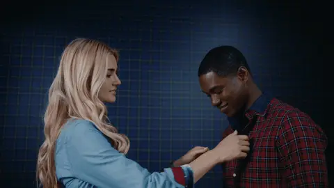 A woman straightens the collar of a smiling man wearing a red plaid shirt.