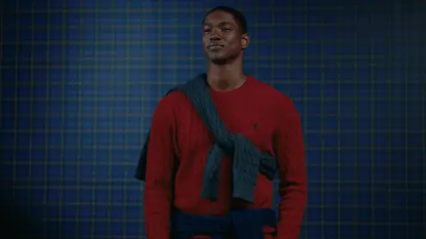 A man in red and green knit layers catches a bright blue sweater and gathers it in his hands.