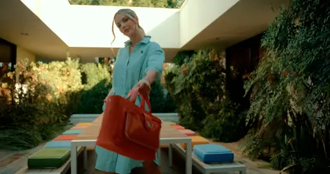 A woman in a teal outfit carries an orange bag along a colorful modern patio.