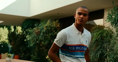 A man in a white striped polo stands on a warm desert patio beside a modern house.