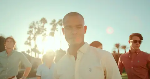 A group in polo shirts walks toward the camera through strong golden lens flare.