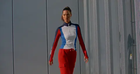 A woman walks in a red, white, and blue track suit beside a modern building.
