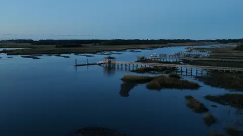 A wide aerial view shows docks crossing blue water between marsh islands at blue hour.