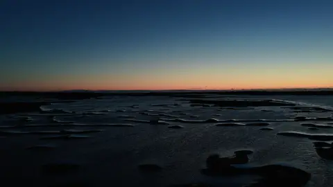 Graphic tidal channels and marsh islands sit beneath a narrow warm horizon at dusk.