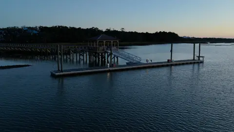 A closer aerial view isolates a long dock and boathouse over dark blue water.