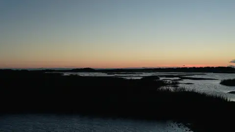 Layered marsh channels form horizontal bands beneath a pale dusk sky.