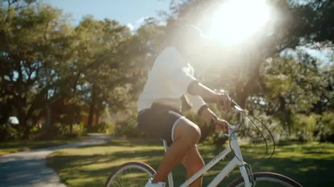 A backlit cyclist crosses a tree-lined resort road through strong morning flare.