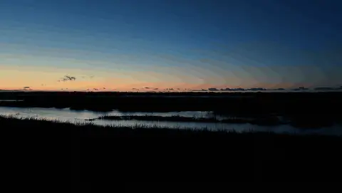A slow aerial move reveals reflective tidal water beneath a blue-hour horizon.