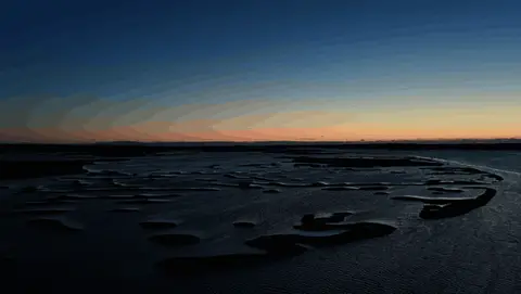 The camera glides across graphic tidal channels and marsh islands at blue hour.