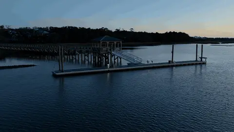 A controlled lateral aerial move circles a dock and boathouse over dark blue water.